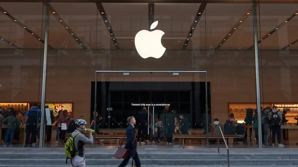 Magasin Apple avec le logo lumineux de la marque au-dessus de l'entrée, des clients à l'intérieur et des passants à l'extérieur.