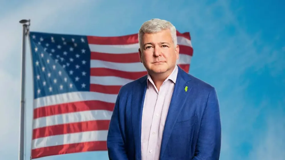 Un homme en costume bleu se tient devant un drapeau américain.