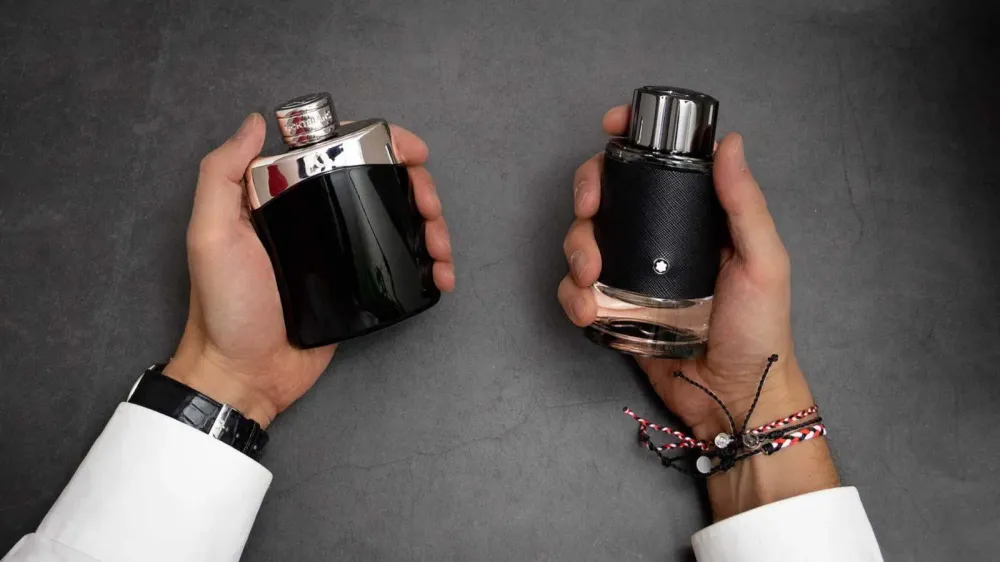 Deux flacons de parfum Montblanc Legend, un noir brillant et un noir texturé, tenus par des mains avec une montre et des bracelets.