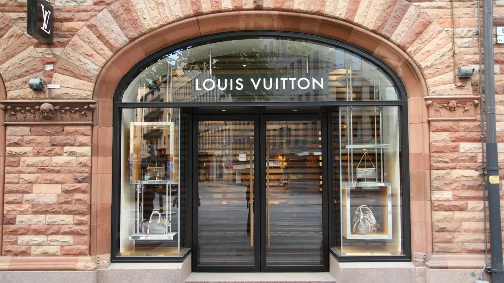 Façade d'un magasin Louis Vuitton avec une grande arche en pierre et des vitrines présentant des sacs à main.