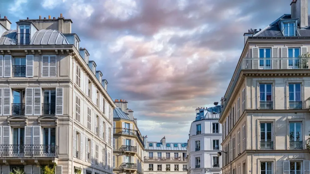 Immeubles parisiens typiques avec des fenêtres à volets et des toits en zinc sous un ciel nuageux.
