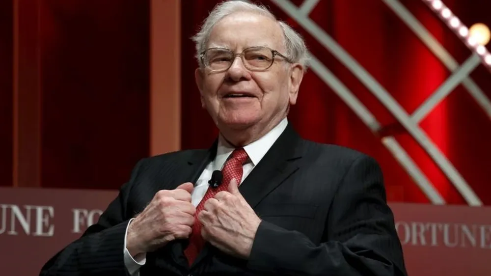 Warren Buffett souriant en costume et cravate rouge.