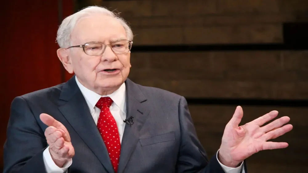 Warren Buffett s'exprimant avec un costume et une cravate rouges, illustrant son implication dans les décisions d'investissement.
