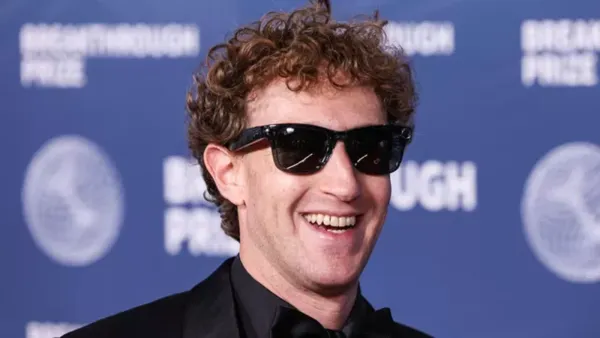 Mark Zuckerberg souriant, portant des lunettes de soleil et un costume noir, devant un fond bleu avec le texte 'Breakthrough Prize'.