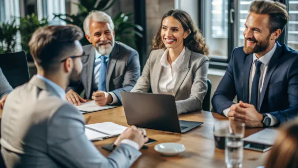 Des professionnels souriants assis autour d'une table de réunion, discutant de l'achat d'un bien immobilier à plusieurs.