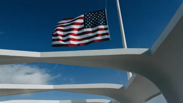 Drapeau américain flottant sur un ciel bleu, encadré par des structures architecturales blanches.