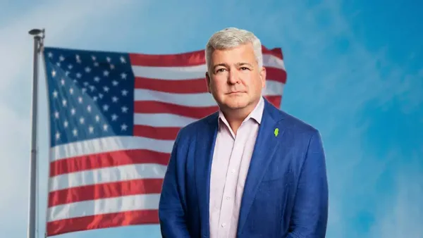 Un homme en costume bleu se tient devant un drapeau américain.