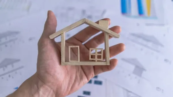 Une main tenant une maquette de maison en bois, symbolisant l'investissement immobilier neuf.