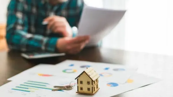 Un homme examine des documents financiers avec une maquette de maison et des clés, symbolisant l'investissement immobilier locatif.