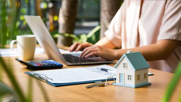 Une personne travaille sur un ordinateur portable à côté d'une maquette de maison, symbolisant l'achat immobilier.