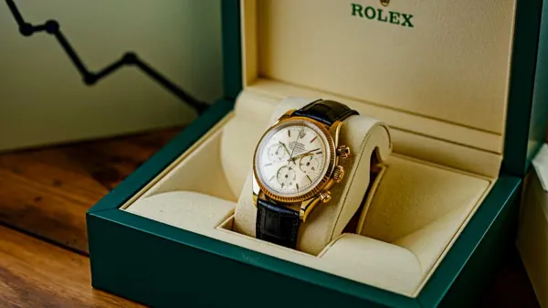 Une montre Rolex en or avec un bracelet en cuir noir est présentée dans un écrin vert.