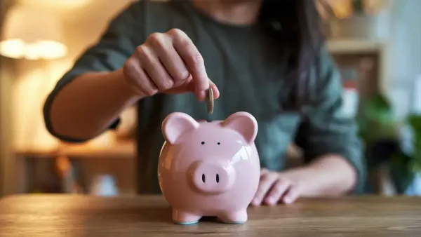 Une personne insère une pièce dans une tirelire rose en forme de cochon.